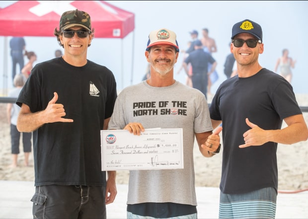 Mark holding a check between 2 men who all give a shaka